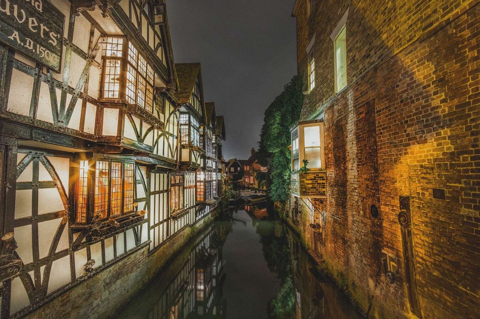 Historic riverside buildings beside a narrow watercourse at night, illustrating planning and flood risk considerations for development near waterways.
